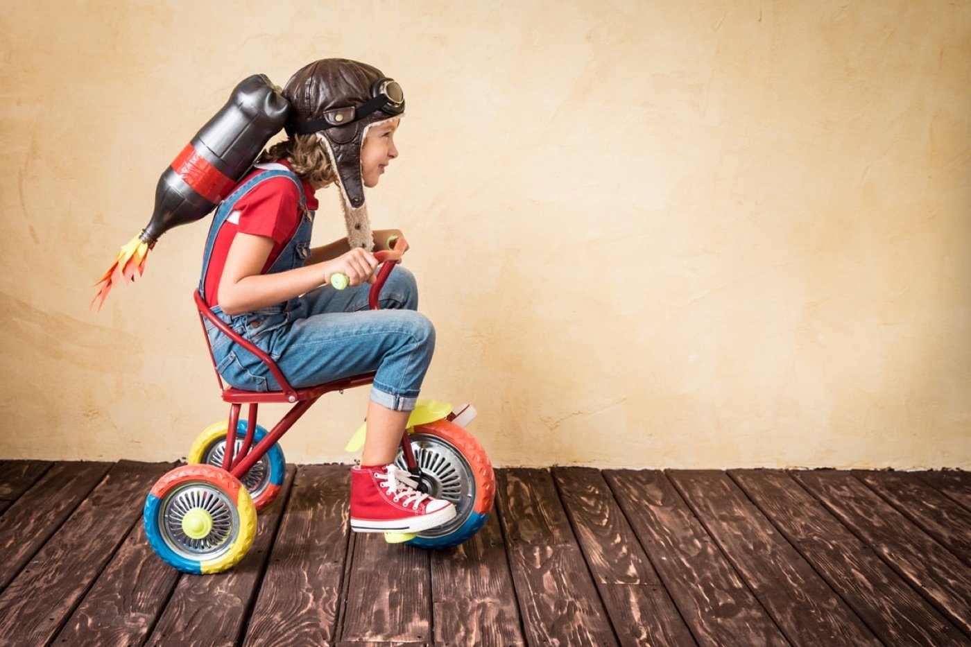 Child riding a tricycle with a toy rocket, imagining flight
