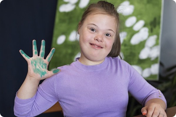 Smiling girl holding up a hand covered in green paint